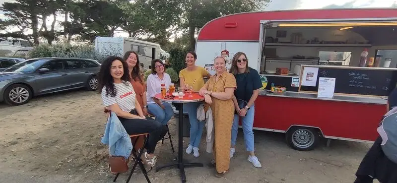 Groupe d'amies souriantes posant devant la caravane crêpes rouge et blanche