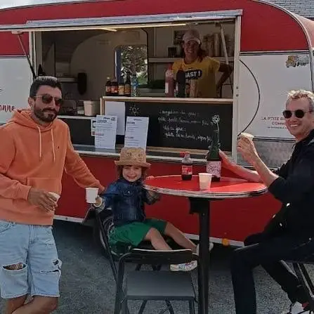 Deux adultes et un enfant au chapeau de paille autour d'un mange-debout devant la caravane crêpes